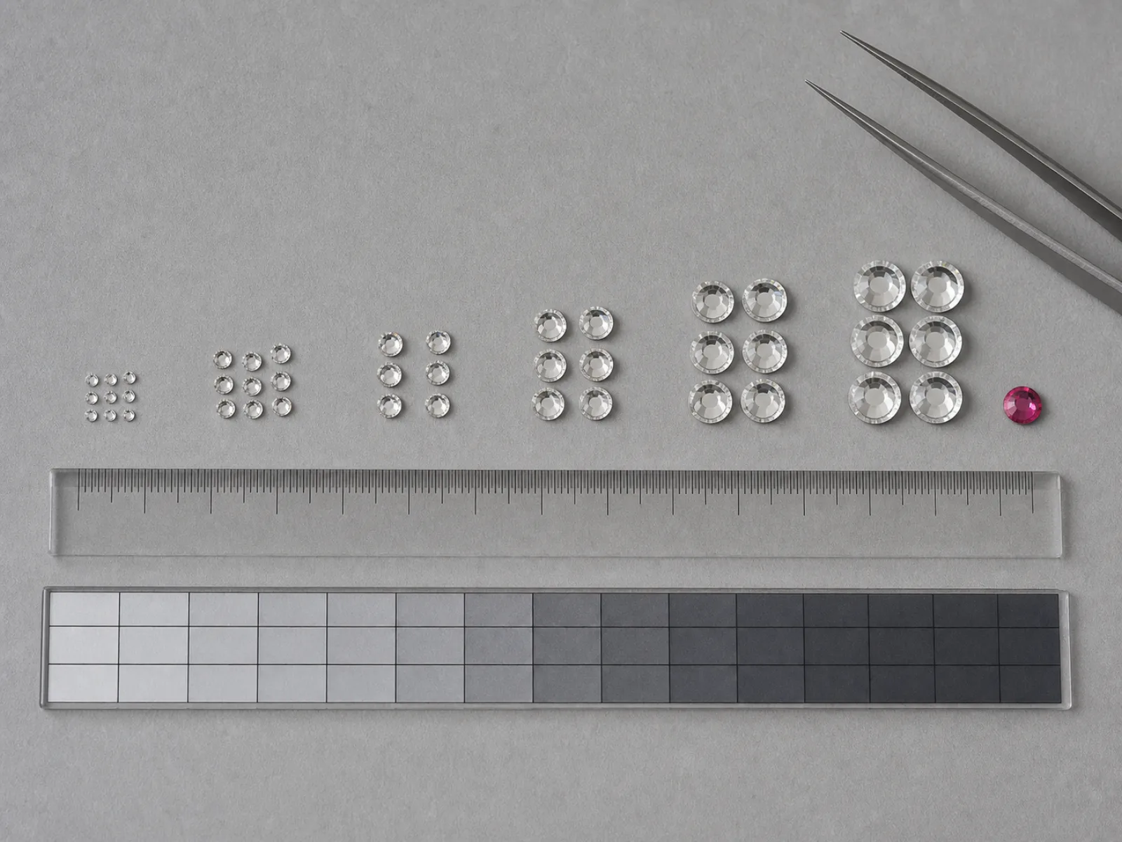 Illustrative macro photograph of crystal rhinestones arranged beside a millimeter ruler and calibration grid