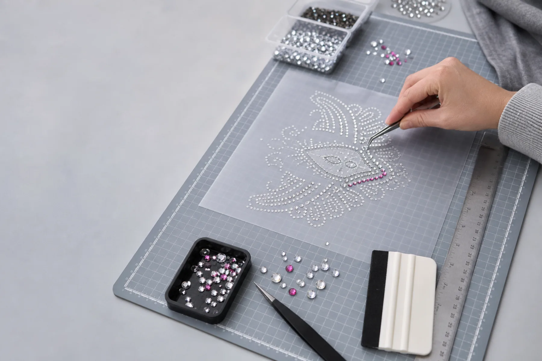 Illustrative overhead studio view of a rhinestone craft workbench with a dotted flower template